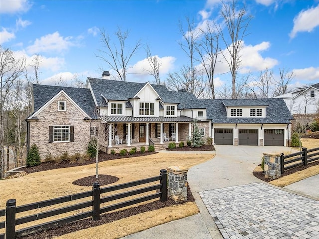 modern inspired farmhouse featuring a fenced front yard, an attached garage, covered porch, driveway, and a standing seam roof