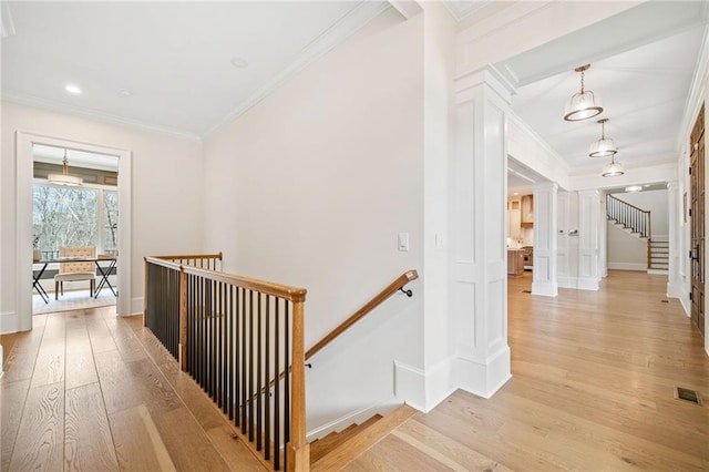 hallway with light wood-style flooring, visible vents, an upstairs landing, and ornamental molding