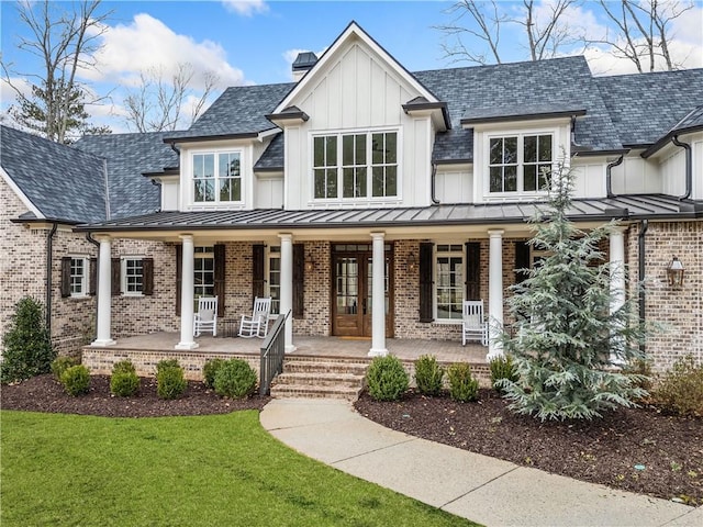 modern farmhouse featuring a standing seam roof, a chimney, covered porch, brick siding, and board and batten siding