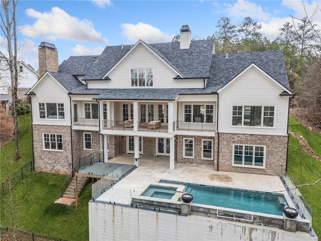 back of property featuring a chimney, a patio area, a lawn, a balcony, and an in ground hot tub