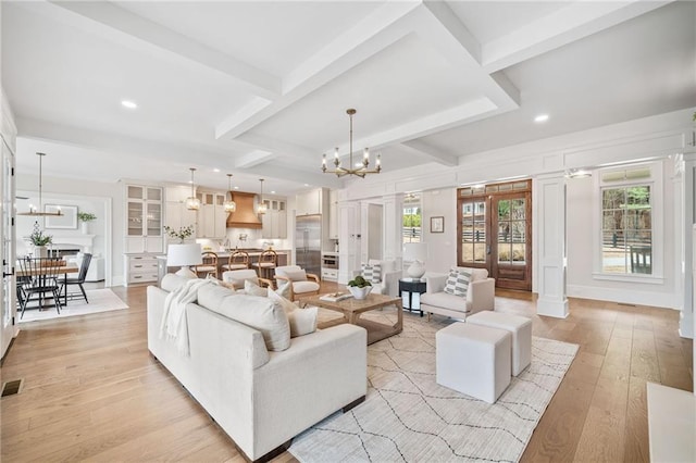 living room with light wood-style flooring, visible vents, a notable chandelier, coffered ceiling, and beamed ceiling