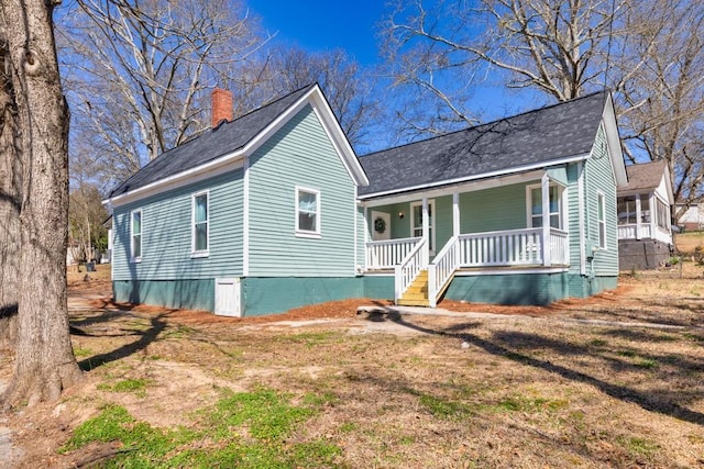 view of front of home with covered porch, a chimney, and a shingled roof