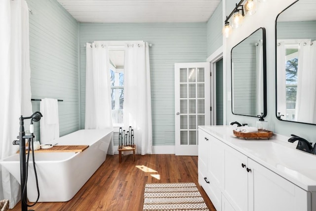 bathroom featuring wood finished floors, healthy amount of natural light, a freestanding bath, and double vanity