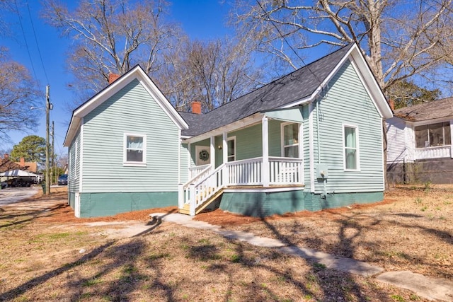 view of front of property with covered porch, a chimney, and a shingled roof