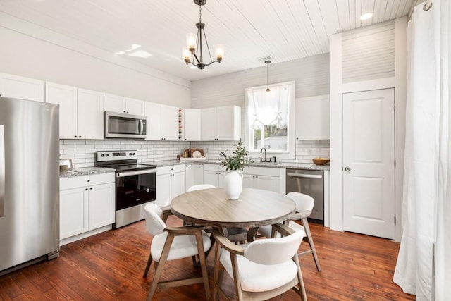 kitchen with appliances with stainless steel finishes, a sink, a chandelier, decorative backsplash, and dark wood-style floors