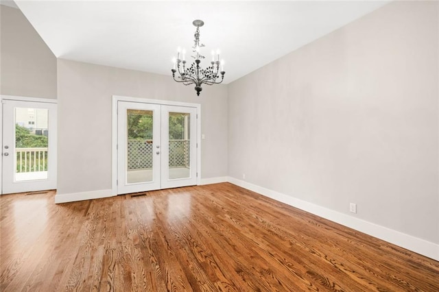 empty room with french doors, a notable chandelier, plenty of natural light, and wood-type flooring