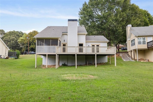 rear view of property with a trampoline, a deck, a yard, and a sunroom