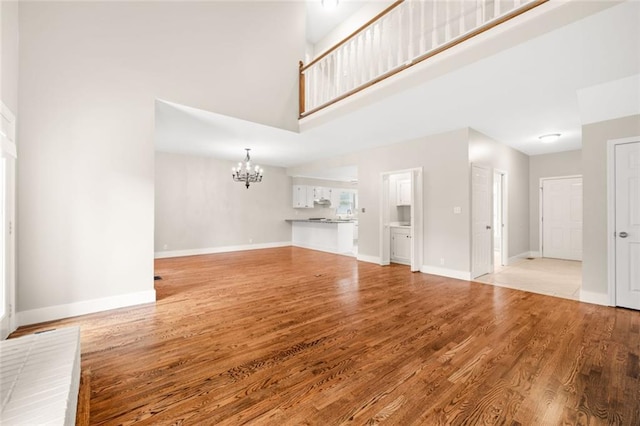 unfurnished living room featuring an inviting chandelier, light wood-type flooring, and a high ceiling