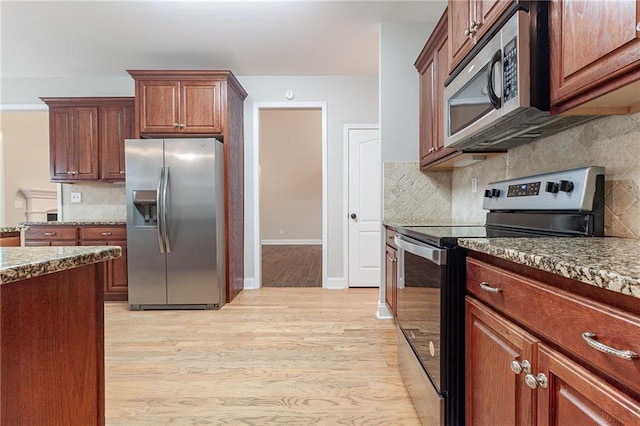 kitchen with tasteful backsplash, light stone countertops, appliances with stainless steel finishes, and light hardwood / wood-style flooring