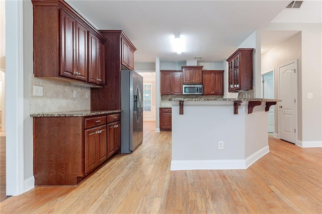 kitchen featuring light stone countertops, light hardwood / wood-style floors, a kitchen bar, decorative backsplash, and appliances with stainless steel finishes