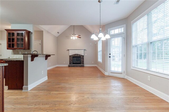 unfurnished living room with ceiling fan with notable chandelier, light hardwood / wood-style flooring, a stone fireplace, and plenty of natural light