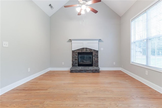 unfurnished living room with ceiling fan, vaulted ceiling, a stone fireplace, and light hardwood / wood-style flooring