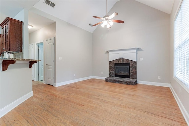 unfurnished living room with a stone fireplace, sink, vaulted ceiling, light hardwood / wood-style flooring, and ceiling fan