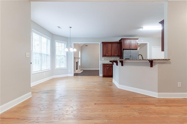 kitchen with kitchen peninsula, a kitchen breakfast bar, tasteful backsplash, light hardwood / wood-style flooring, and stainless steel refrigerator