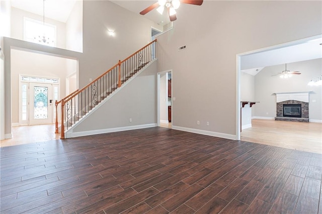 unfurnished living room with ceiling fan, a stone fireplace, and a high ceiling