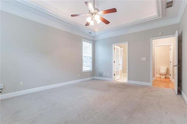 unfurnished bedroom featuring connected bathroom, ceiling fan, a raised ceiling, crown molding, and light colored carpet