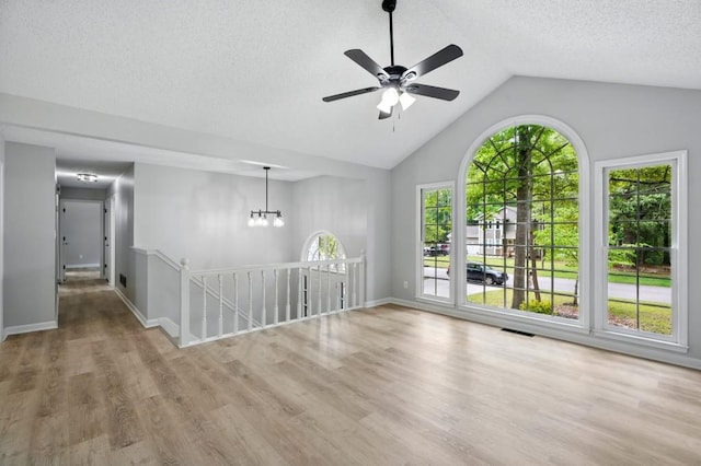 empty room featuring a textured ceiling, ceiling fan with notable chandelier, baseboards, wood finished floors, and lofted ceiling