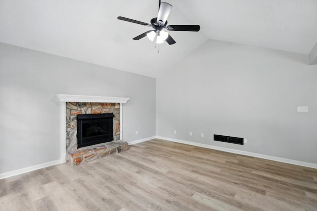 unfurnished living room with ceiling fan, a stone fireplace, visible vents, vaulted ceiling, and wood finished floors