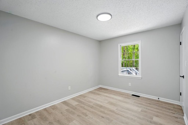 empty room featuring light wood-style floors, a textured ceiling, baseboards, and visible vents