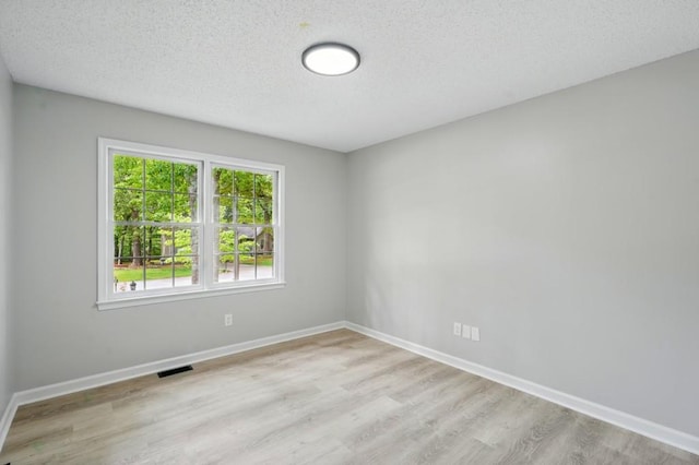 spare room featuring visible vents, a textured ceiling, light wood-style flooring, and baseboards