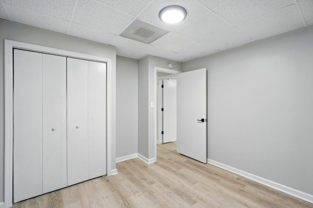 unfurnished bedroom featuring visible vents, a closet, baseboards, a paneled ceiling, and light wood finished floors