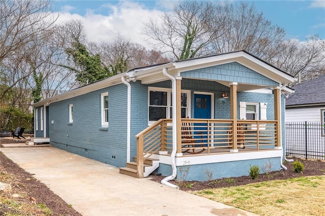 view of front facade with a porch, crawl space, brick siding, and fence