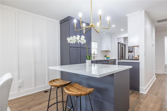 kitchen featuring a breakfast bar area, visible vents, a decorative wall, freestanding refrigerator, and light wood-type flooring