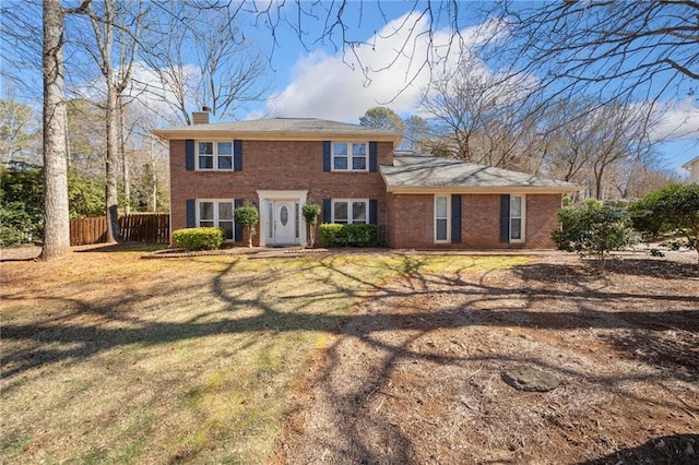 colonial inspired home featuring brick siding, fence, a chimney, and a front lawn