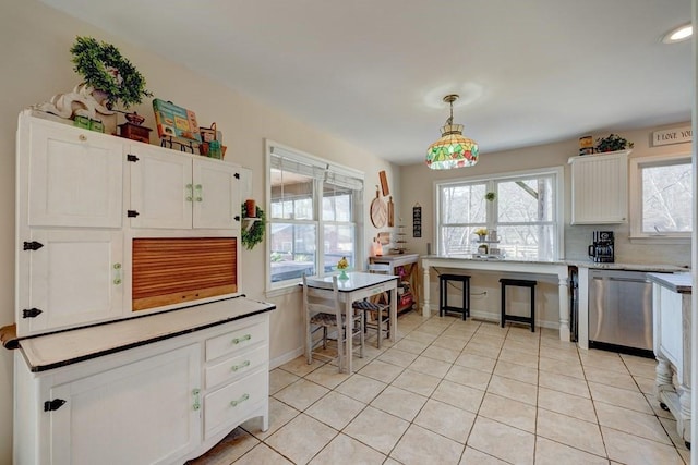 kitchen featuring light tile patterned flooring, hanging light fixtures, stainless steel dishwasher, white cabinets, and backsplash