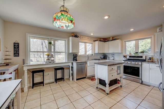 kitchen with decorative light fixtures, stainless steel appliances, white cabinets, and a kitchen island