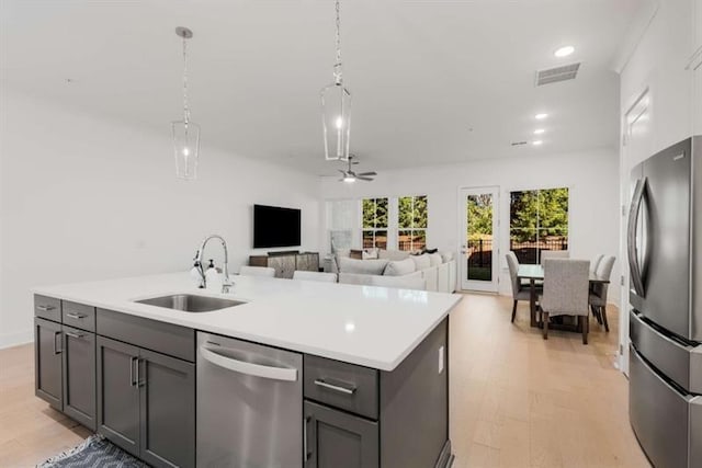 kitchen featuring appliances with stainless steel finishes, a sink, light countertops, an island with sink, and pendant lighting