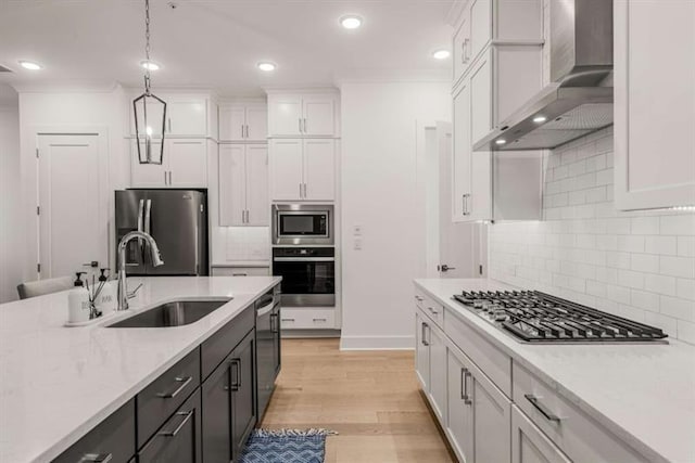 kitchen featuring pendant lighting, wall chimney range hood, white cabinets, a sink, and appliances with stainless steel finishes
