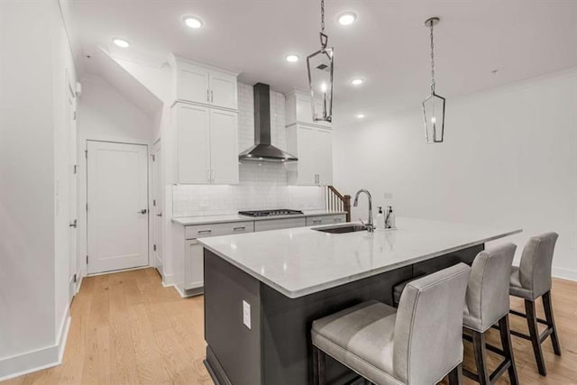 kitchen featuring stainless steel gas cooktop, a kitchen bar, wall chimney exhaust hood, a sink, and light wood finished floors