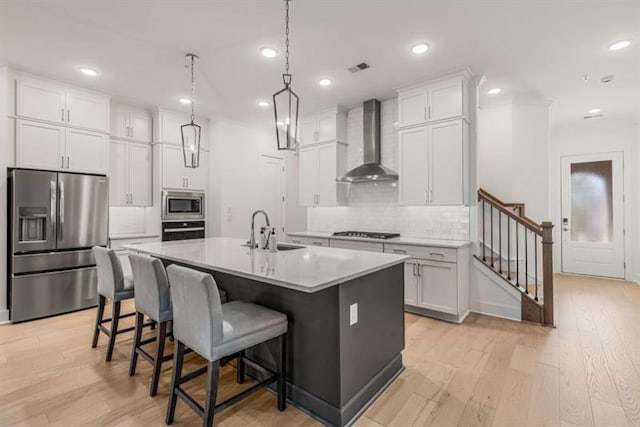 kitchen with wall chimney range hood, appliances with stainless steel finishes, tasteful backsplash, light wood-type flooring, and a sink