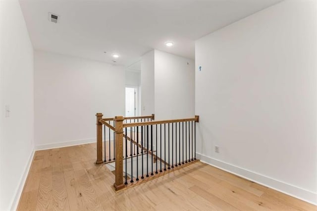 corridor with visible vents, baseboards, recessed lighting, light wood finished floors, and an upstairs landing