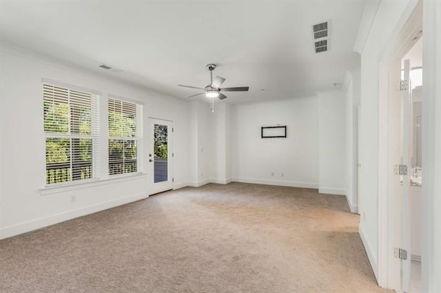 spare room featuring light colored carpet, ceiling fan, visible vents, and a healthy amount of sunlight