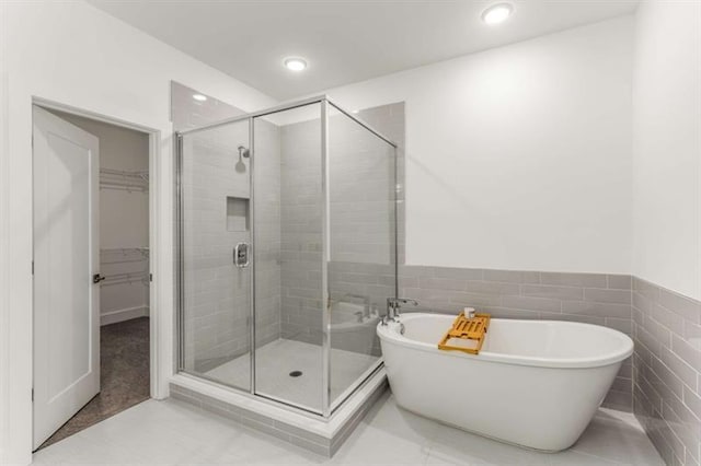 full bath with a walk in closet, tile walls, a shower stall, a soaking tub, and recessed lighting