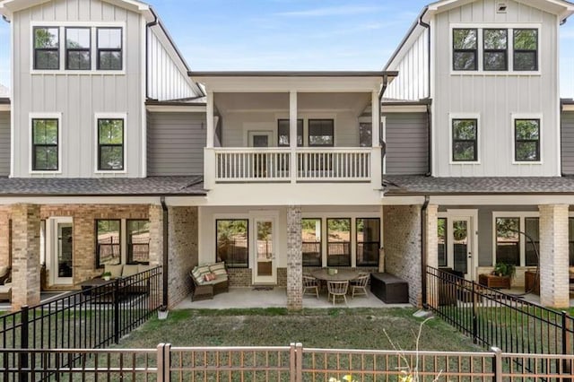 back of property with a balcony, a fenced backyard, brick siding, board and batten siding, and a patio area