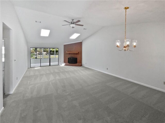 unfurnished living room featuring baseboards, carpet floors, a brick fireplace, lofted ceiling with skylight, and ceiling fan with notable chandelier