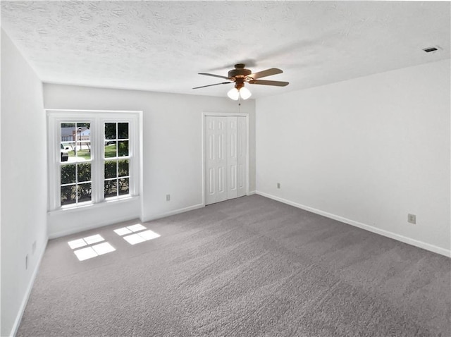 carpeted spare room with visible vents, baseboards, a ceiling fan, and a textured ceiling