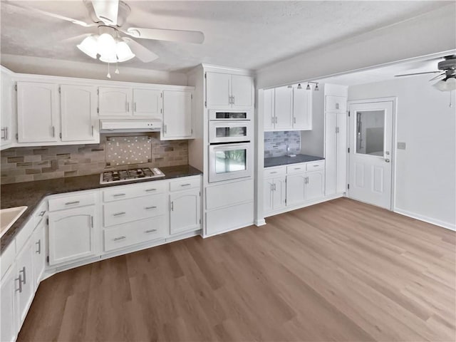 kitchen with ceiling fan, dark countertops, under cabinet range hood, white cabinetry, and stainless steel gas stovetop