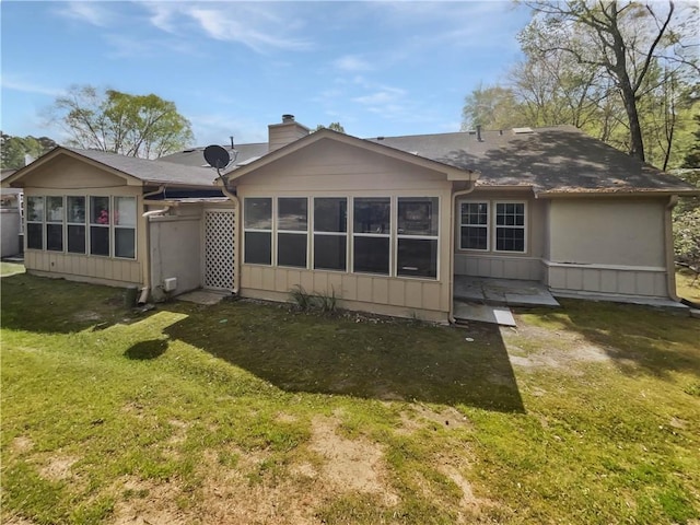 rear view of property with a sunroom, a lawn, and a chimney