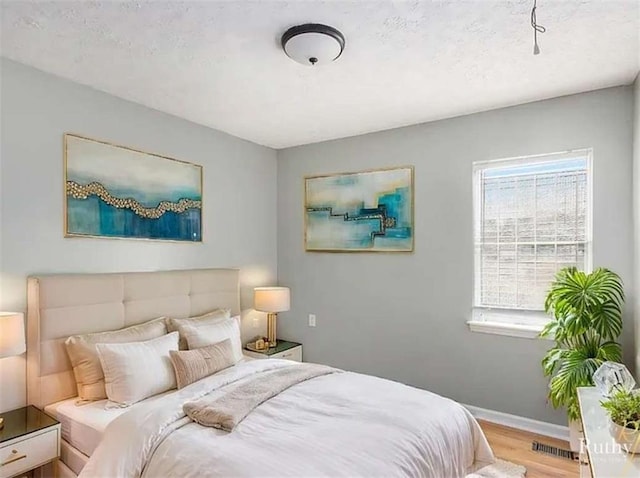 bedroom featuring visible vents, a textured ceiling, baseboards, and wood finished floors