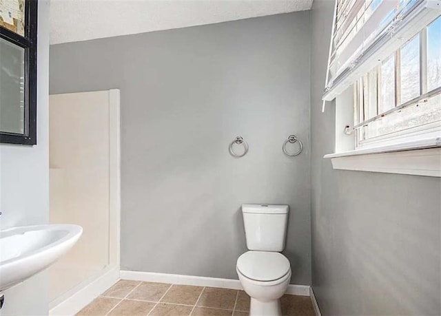 bathroom with tile patterned flooring, toilet, baseboards, and a sink