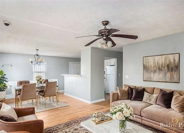 living area with ceiling fan with notable chandelier, light wood-type flooring, and baseboards