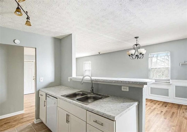 kitchen with a sink, decorative light fixtures, white dishwasher, light wood finished floors, and light countertops