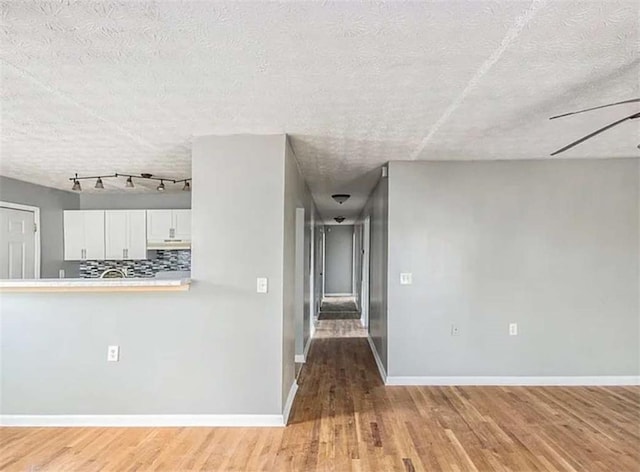 interior space featuring ceiling fan, a textured ceiling, light wood-type flooring, and baseboards