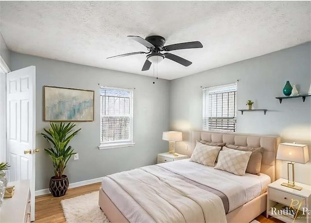 bedroom with baseboards, multiple windows, a textured ceiling, and wood finished floors