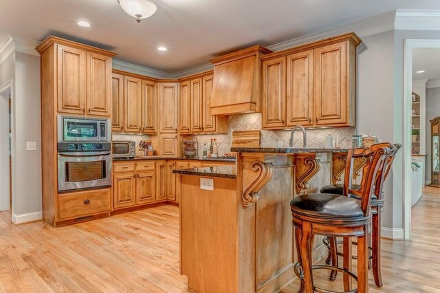 27 Bluff Mountain Dr SW, Rome, GA 30165 - kitchen with stainless steel appliances, light wood-style floors, a kitchen bar, dark stone countertops, and crown molding