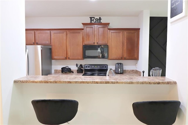 3130 Haynes Park Dr, Lithonia, GA 30038 - kitchen with black appliances, a breakfast bar, brown cabinets, and light countertops